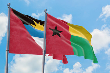 Guinea Bissau and Antigua and Barbuda flags waving in the wind against white cloudy blue sky together. Diplomacy concept, international relations.