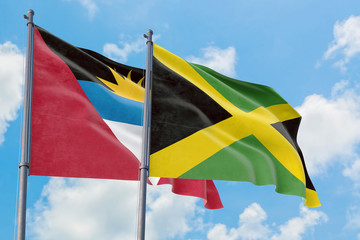 Jamaica and Antigua and Barbuda flags waving in the wind against white cloudy blue sky together. Diplomacy concept, international relations.