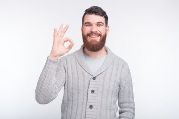 Naklejka premium Smiling bearded hipster is showing ok gesure on white background.