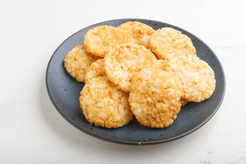 Traditional japanese rice chips cookies with honey and soy sauce on a blue ceramic plate on a white wooden background. side view.