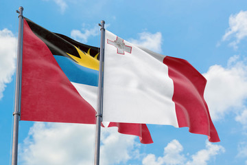 Malta and Antigua and Barbuda flags waving in the wind against white cloudy blue sky together. Diplomacy concept, international relations.