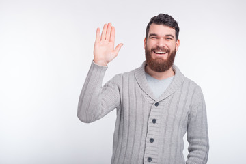 Cheeerful young bearded man is saying hi making hello gesture, and smiling at the camera.