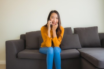 Portrait young asian woman using smart mobile phone on sofa with pillow in living room