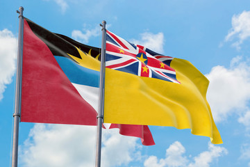 Niue and Antigua and Barbuda flags waving in the wind against white cloudy blue sky together. Diplomacy concept, international relations.