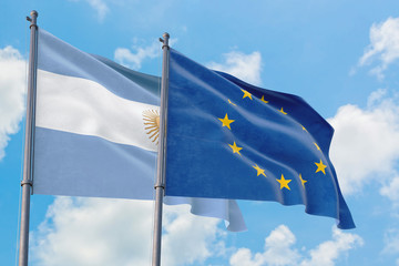 European Union and Argentina flags waving in the wind against white cloudy blue sky together....