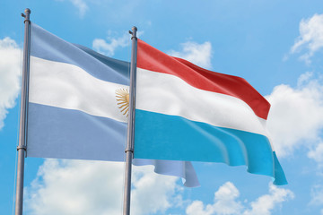 Luxembourg and Argentina flags waving in the wind against white cloudy blue sky together. Diplomacy concept, international relations.