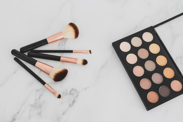 group of make-up brushes for face and eyes next to palette with neutral nude tones