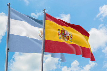 Spain and Argentina flags waving in the wind against white cloudy blue sky together. Diplomacy concept, international relations.