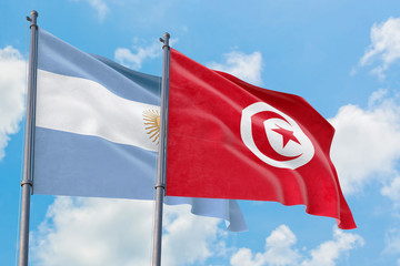 Tunisia and Argentina flags waving in the wind against white cloudy blue sky together. Diplomacy concept, international relations.