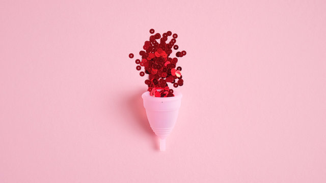 Reusable menstrual cup filled with red confetti on pink background. Alternative menstrual hygiene product. Critical days, menstruation cycle, female healthcare concept. Flat lay, top view