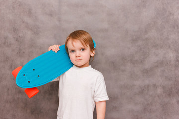 Little boy wearing a casual outfit, hold his skateboard on his shoulder,standing on a gray background. sale concept sports equipment © habrovich