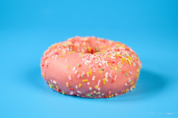 Pink iced donut on blue background. Sweet dessert top view .