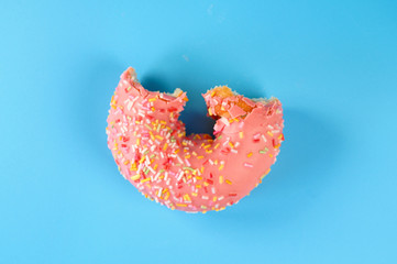 Pink frosted donut with colorful sprinkles with bite missing. On blue background .