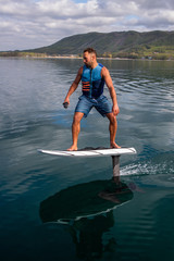 Man riding an electric hydrofoil foil board on a lake with a life jacket