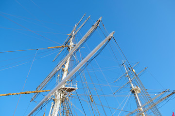 Yards and masts of a romantic classic sailing ship, visible shrouds, stays and complex rigging, blue sky in the background.
