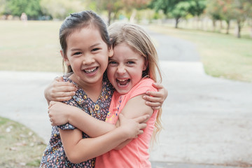 Happy and healthy mixed race multiethnic young little girls hugging and smiling in the park, best...