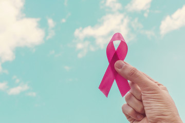Hand holding pink ribbon over blue sky, world cancer day, breast cancer awareness, october pink concept, world cancer day