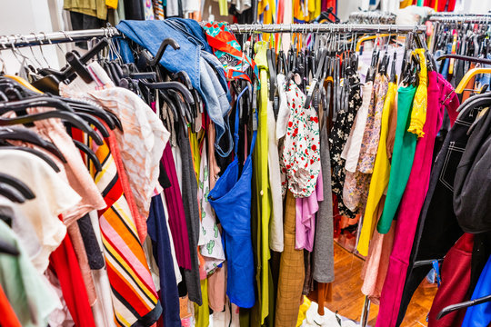 Crowded clearance section in a clothing store, with various colorful garments placed tightly on racks in no particular order; fast fashion concept