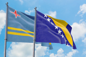 Bosnia Herzegovina and Aruba flags waving in the wind against white cloudy blue sky together. Diplomacy concept, international relations.