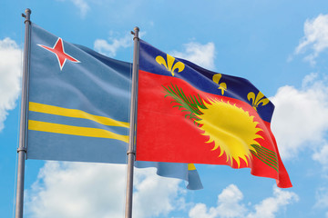 Guadeloupe and Aruba flags waving in the wind against white cloudy blue sky together. Diplomacy concept, international relations.