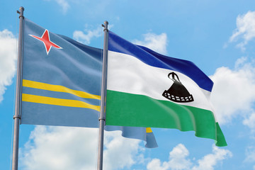 Lesotho and Aruba flags waving in the wind against white cloudy blue sky together. Diplomacy concept, international relations.