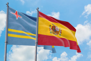 Spain and Aruba flags waving in the wind against white cloudy blue sky together. Diplomacy concept, international relations.