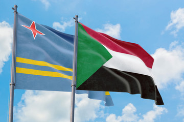 Sudan and Aruba flags waving in the wind against white cloudy blue sky together. Diplomacy concept, international relations.