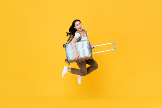 Excited beautiful Asian woman tourist jumping with luggage