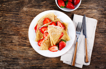 Crepes with strawberries onwooden background, top view.