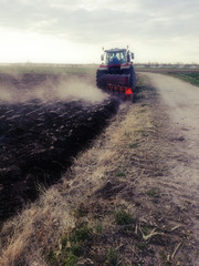 Tractor in the sunset next to dirt road. Agricultural work. Plowing with a moldboard plow. Rural scene of countryside environment in the center of Spain.