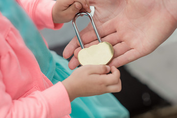 Fototapeta premium unusual metal gold closed lock in hands, a little girl passes the lock to a large adult hand