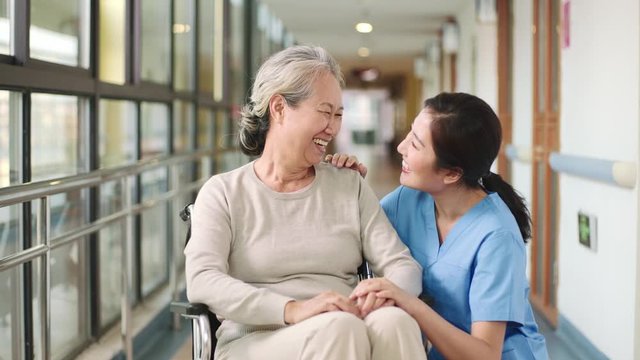 friendly staff of nursing home talking chatting with senior asian woman in hallway