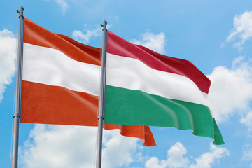 Hungary and Austria flags waving in the wind against white cloudy blue sky together. Diplomacy concept, international relations.