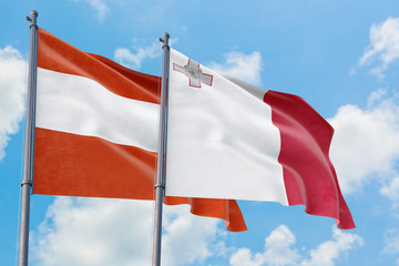 Malta and Austria flags waving in the wind against white cloudy blue sky together. Diplomacy concept, international relations.