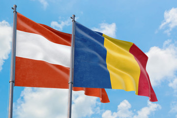 Romania and Austria flags waving in the wind against white cloudy blue sky together. Diplomacy...