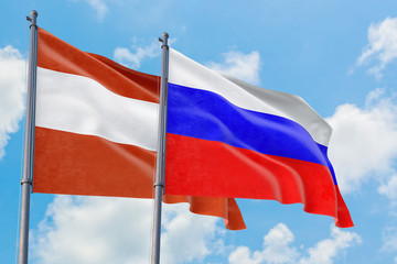 Russia and Austria flags waving in the wind against white cloudy blue sky together. Diplomacy concept, international relations.