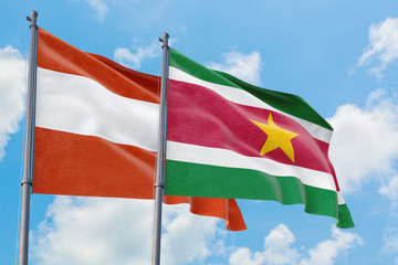 Suriname and Austria flags waving in the wind against white cloudy blue sky together. Diplomacy concept, international relations.