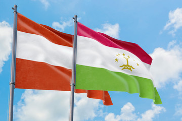 Tajikistan and Austria flags waving in the wind against white cloudy blue sky together. Diplomacy concept, international relations.