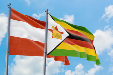 Zimbabwe and Austria flags waving in the wind against white cloudy blue sky together. Diplomacy concept, international relations.