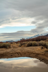 California valley view with snowy Sierra Nevada mountain range reflected in rain puddle in dirt road