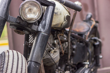 Fototapeta premium Detail of front part of retro vintage style motorcycle, with metal-protected headlight and modifications in engine, tank, seat and suspension showing rust throughout the body