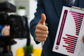 Male in suit and tie show confirm sign arm making promo videoblog or photo session in office camcorder to tripod closeup. Vlogger promotion selfie solution or finance advisor management information © H_Ko