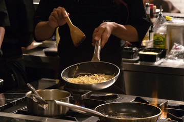 Chef cooking spaghetti with bacon, garlic, olive oil and chili in a open kitchen; customer can see they cooking at food counter. 