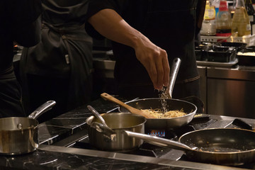 Chef cooking spaghetti with bacon, garlic, olive oil and chili in a open kitchen; customer can see they cooking at food counter. 
