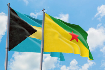 French Guiana and Bahamas flags waving in the wind against white cloudy blue sky together. Diplomacy concept, international relations.