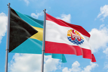 French Polynesia and Bahamas flags waving in the wind against white cloudy blue sky together. Diplomacy concept, international relations.