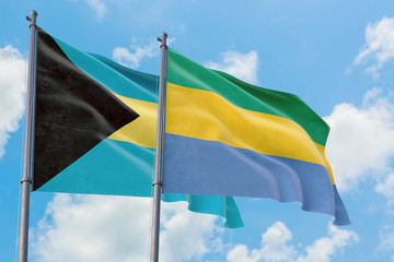 Gabon and Bahamas flags waving in the wind against white cloudy blue sky together. Diplomacy...