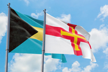 Guernsey and Bahamas flags waving in the wind against white cloudy blue sky together. Diplomacy concept, international relations.