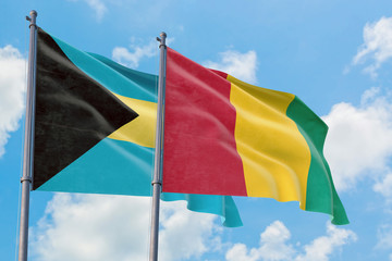 Guinea and Bahamas flags waving in the wind against white cloudy blue sky together. Diplomacy concept, international relations.