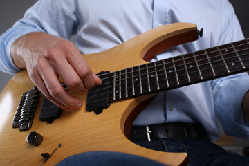 Male arms holding and playing classic shape wooden electric guitar closeup. Six stringed learning...